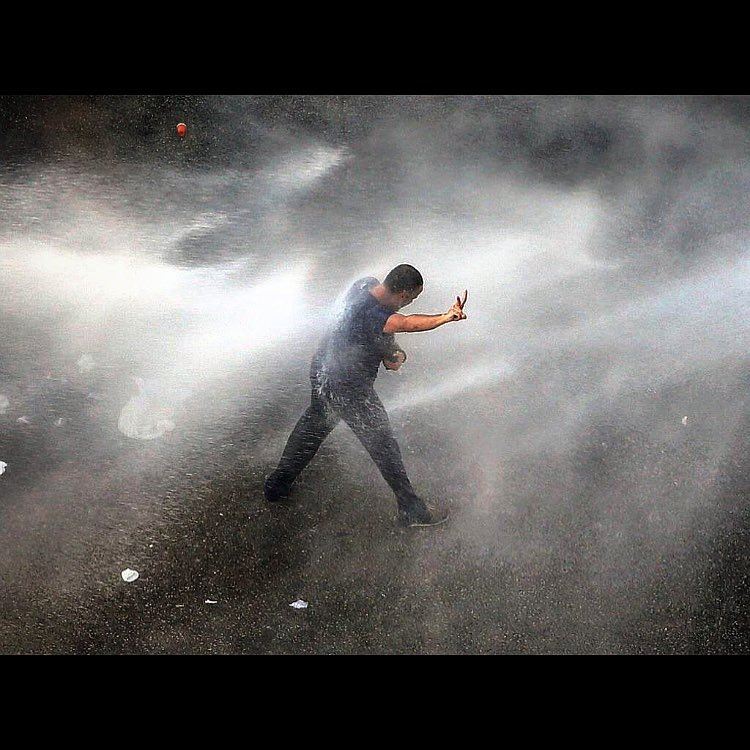 A Lebanese activist is sprayed with water, by riot police, while he tries...