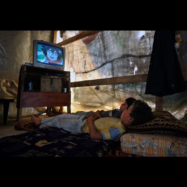 Syrian refugee boys watch television inside their family's tent at a...