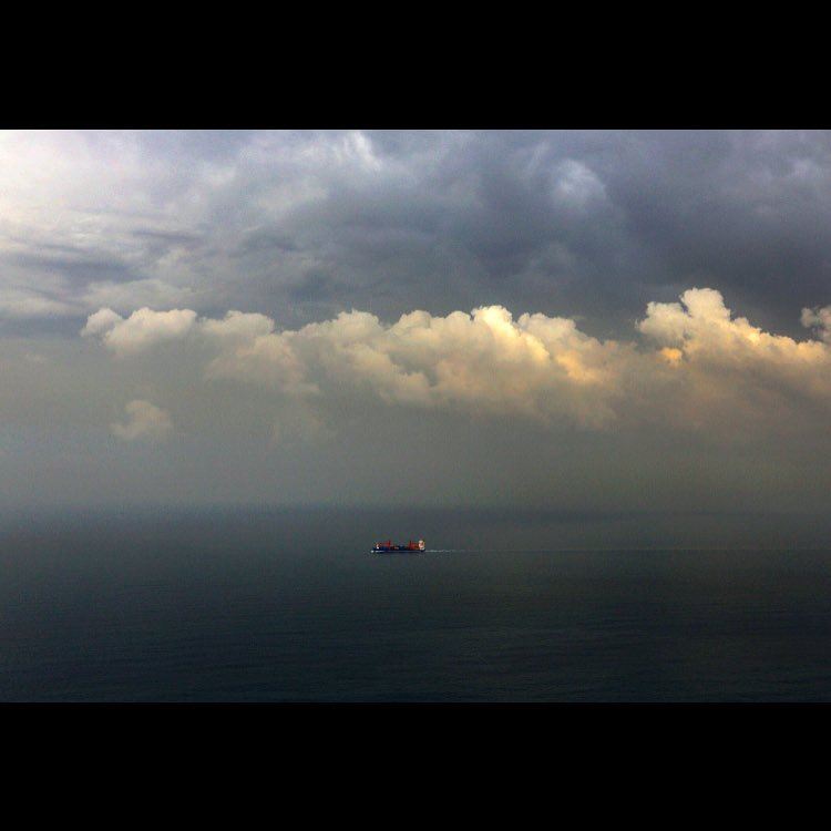 A cargo ship navigates in the Mediterranean Sea under heavy clouds along...