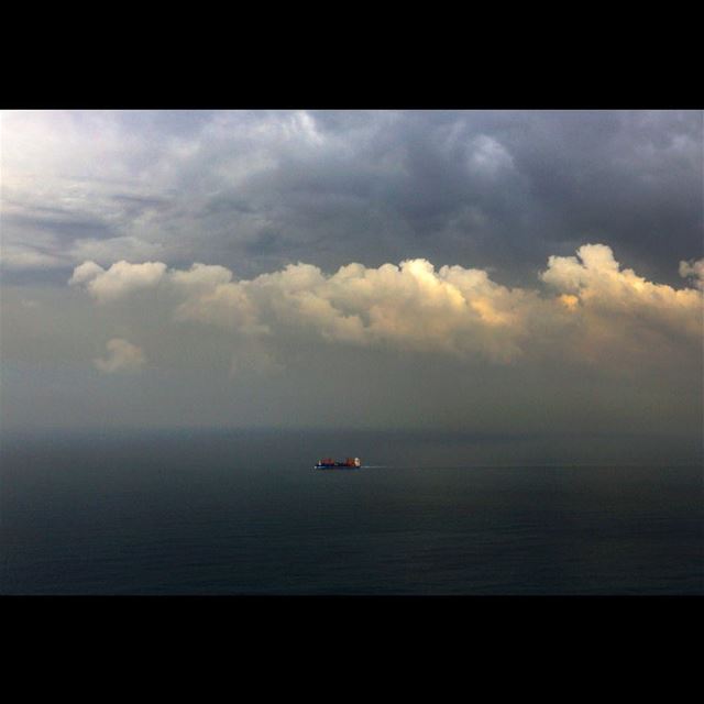 A cargo ship navigates in the Mediterranean Sea under heavy clouds along...