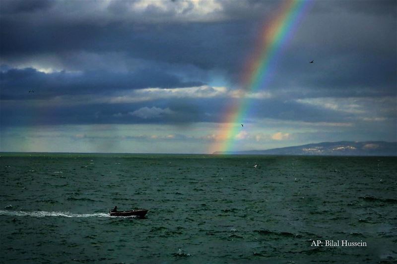 A Lebanese fisherman in his boat on the Mediterranean Sea as a rainbow...