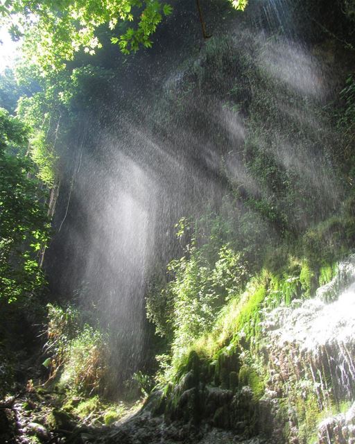 A waterfall looking like a curtain with the sun rays cutting through it ...
