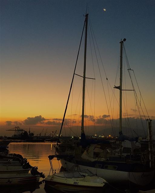 Dusk flaming color with the crescent moon and masts of a sailing boat in... (Port of Tripoli)