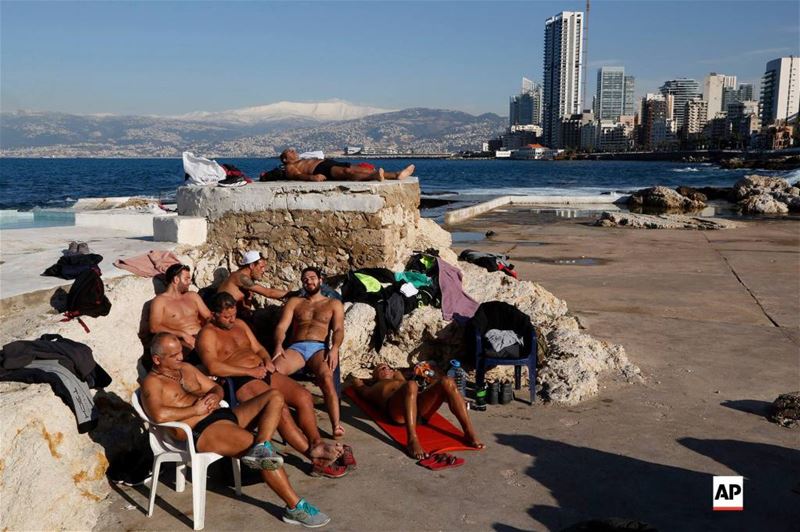 Men sunbathing by the Mediterranean sea, as snow is seen on the background covering the mountains, in Beirut, Lebanon