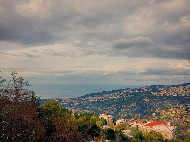 Snow residue over red tile rooftops.  mountain  clouds  sea  trees  houses...