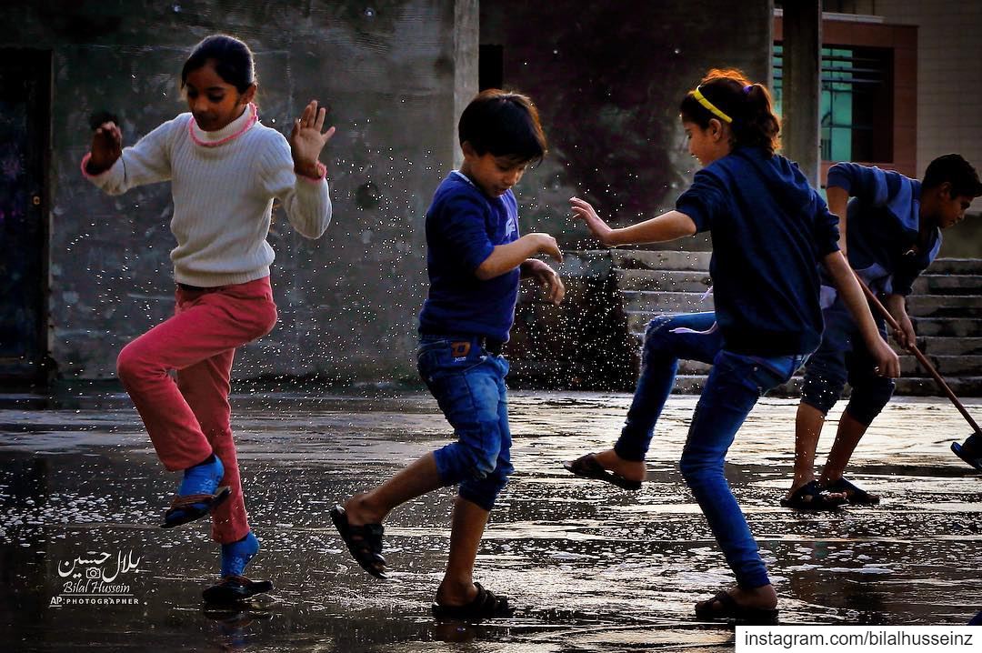 Syrian refugee children play in rain water in a refugee settlement in...
