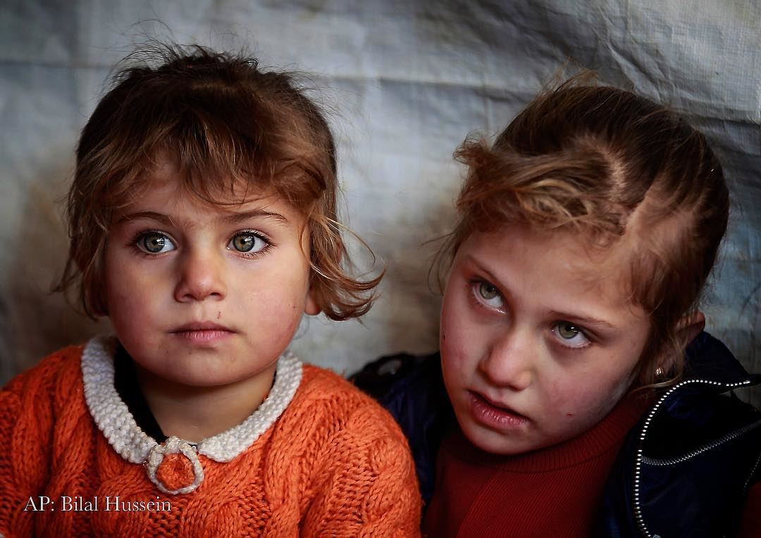 Syrian refugee Eman al-Aqraa, 8, right, and her sister Fatima, 4, listen...
