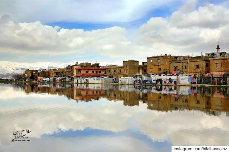 Syrian refugee's tents are reflected in a pool of rain water at a refugee...